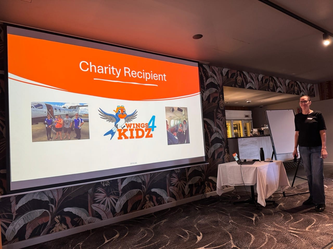The host beside a slide titled Charity Recipient